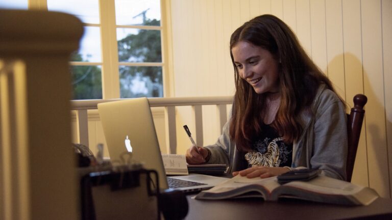 Girl smiles while studying with textbooks and laptop