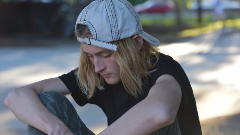 Teenage boy with backwards cap crosses his hands and looks down.