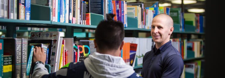Student and teacher choose a book from library shelf