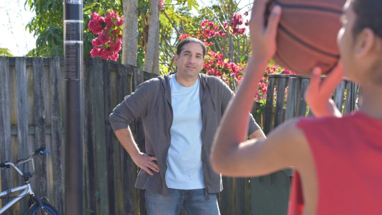 Dad smiling watching son shoot a ball at the basketball hoop